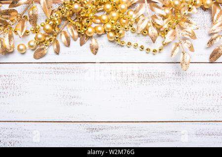 Golden colored Christmas decorations on a white wood background with copy space. Leaves, garland, berries etc. Stock Photo