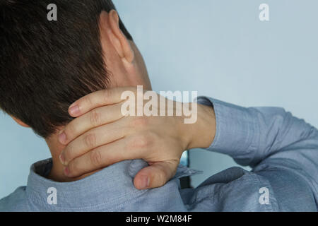 young man is holding his neck. the concept of health, pain in the neck. The patient complains of a sore neck. instability of the vertebrae. fatigue at Stock Photo