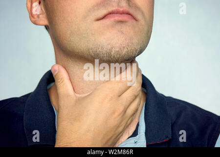 people, healthcare and problem concept - unhappy man touching his neck and suffering from throat pain over blue background. Stock Photo