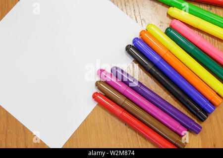 A set of colored markers and a sheet of white paper on the table. Stock Photo