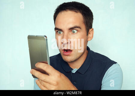 young man looks at the phone and is surprised by what he saw. Puzzled frightened expression on the face of a guy reading the news on the phone Stock Photo