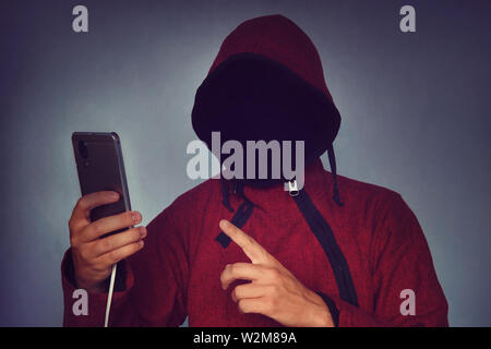 Faceless unrecognizable hooded person using mobile phone, identity theft and technology crime concept, selective focus on body. hacking a smartphone Stock Photo