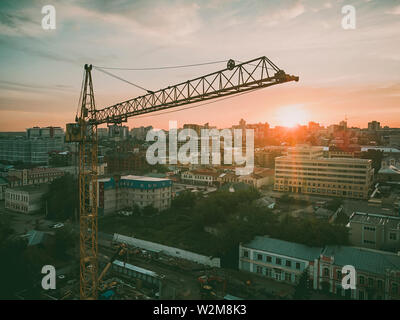 Building site with high-rise block under construction in an urban environment dominated by a large industrial crane silhouetted against a cloudy blue Stock Photo