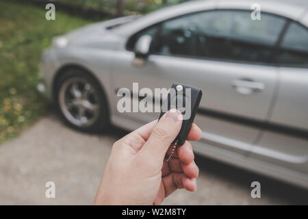 Male car owner switches off the alarm system and unlocks the doors of the car using remote control keys on a parking background. Man starts the Stock Photo