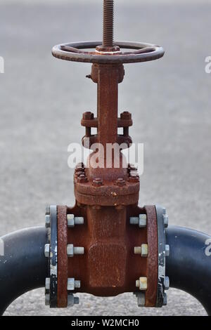 Huge rusty industrial wheel valve bolted to large bore pipes. Stock Photo