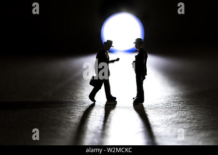 Silhouette of two business figurine walking towards each other in front of a small flashlight Stock Photo