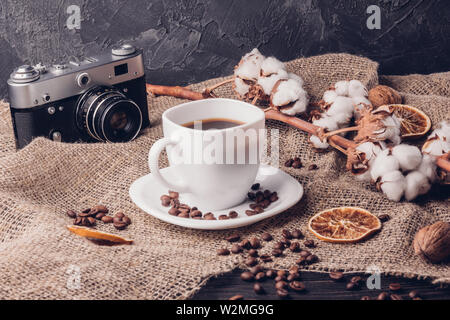 Cup of coffee and coffee beans on a wooden table next to a retro camera and cotton on a branch Stock Photo