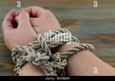 Woman's hands tied with an old rope, the rope is gray with age and unraveling at the ends. It is possible to interpret the picture as torture. Stock Photo