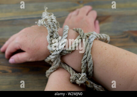 Woman's hands tied with an old rope, the rope is gray with age and unraveling at the ends. It is possible to interpret the picture as torture. Stock Photo