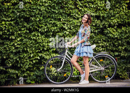 Beautiful woman with her bike standing against hedge Stock Photo