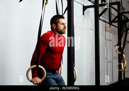 Athletic man doing exercises with gymnastic rings in gym Stock Photo
