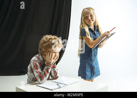 Boy and girl preparing for school after a long summer break. Back to school. Little caucasian models making homework together on studio background. Childhood, education, holidays or homework concept. Stock Photo