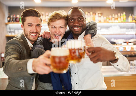 Three men as best friends celebrate hilariously with beer on a pub crawl Stock Photo