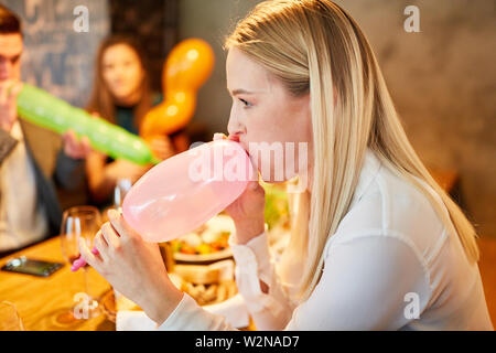 Young woman and friends together while inflating balloons at a party Stock Photo