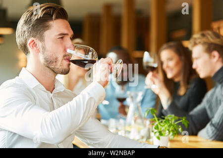 Young man is drinking a glass of red wine together with friends in the restaurant Stock Photo