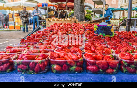 Close up fresh red strawberry berries in plastic containers in wooden box on retail display of farmers market, high angle view. Stock Photo