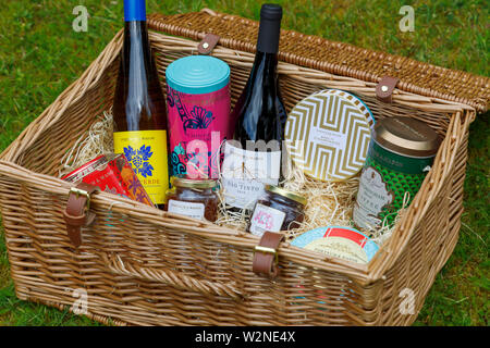 Luxury lifestyle: Fortnum & Mason traditional wicker basket picnic hamper (the Grosvenor Hamper) with open top showing contents outdoors on grass Stock Photo