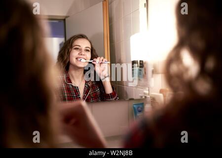 young woman brushing teeth in bathroom at home