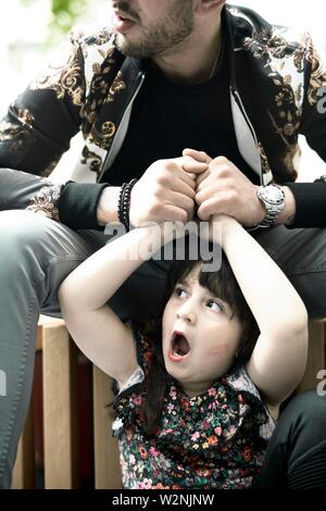 father holding hands of astonished daughter child yawning