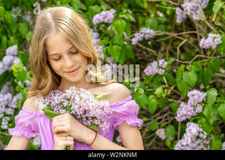 A young blonde girl in a flowered dress holding a bouquet of lilac in his hands. Portrait of a young girl Stock Photo
