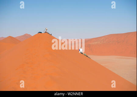 Hikers climbing up a sand dune ridge at Sossusvlei, Namib-Naukluft National Park, Namibia. Stock Photo