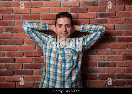 Male portrait Italian, good positive emotions against the background  fire wall in style loft. In klechatoy shirt, jeans and sneakers, urban clothing. Stock Photo