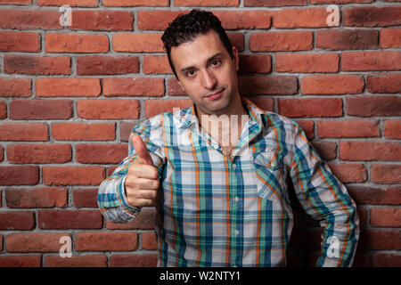 Male portrait Italian, good positive emotions against the background  fire wall in style loft. In klechatoy shirt, jeans and sneakers, urban clothing. Stock Photo