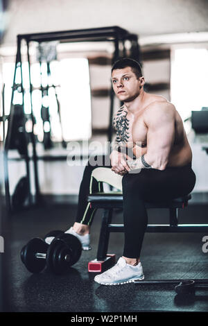 tired male bodybuilder sitting on a bench in a modern gym. Stock Photo