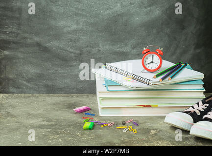 A stack of educational notebooks of books alarm clock on the background of a chalk board. The concept of back to school Stock Photo