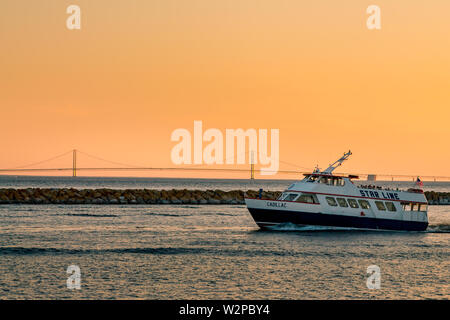 Star Line ferry leaving Mackinac Island harbor in front of the Mackinac Bridge at sunset Stock Photo