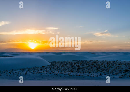 White sands dunes national monument in New Mexico with sun over horizon at sunset with silhouette of Organ Mountains Stock Photo