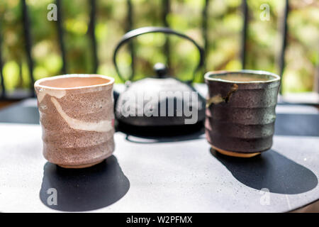 Cast iron teapot on table outside by fence of garden with two cups and Japanese Mino tea cups in morning closeup Stock Photo