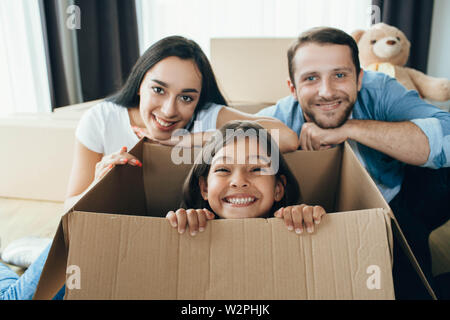 Cute little girl sitting in carton boxes , playing with her parent while moving into new home