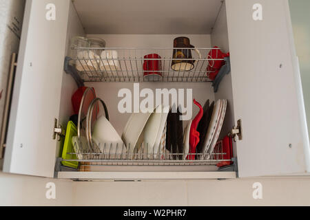 Clean dishes in the drying cupboard.Open kitchen cabinet door with cups, mugs and bowls and plates drying on shelves. Stock Photo