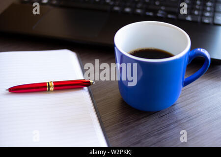 Home office in the morning with sunlight from window. Close up Cup of coffee, Laptop, Notebook with red pen on office desk. Office work concept Stock Photo