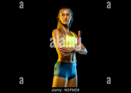 Professional female relay racer training isolated on black studio background in neon light. Woman in sportsuit practicing in running. Healthy lifestyle, sport, workout, motion, action concept. Stock Photo