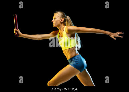 Professional female relay racer training isolated on black studio background in neon light. Woman in sportsuit practicing in running. Healthy lifestyle, sport, workout, motion, action concept. Stock Photo