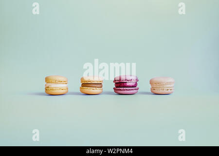 Colored macaroons led by a bright purple on a turquoise background in the center of the picture. Stock Photo