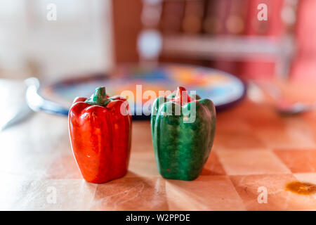Closeup of colorful bell pepper salt and pepper shakes on table by plate in bokeh background Stock Photo