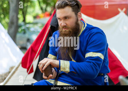Nis, Serbia - June 15. 2019 Knight with a beard in a blue traditional suit sits in front of the tent and plays an old dice game on knight festival Stock Photo