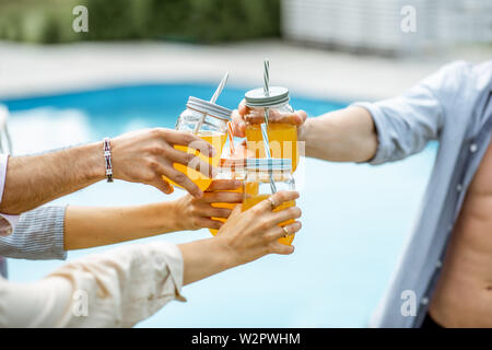 Friends clinking bottles with drinks on the swimming pool, close-up Stock Photo