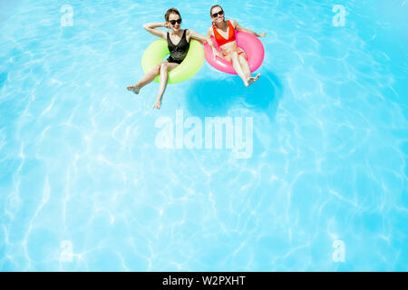 Two women swimming on the inflatable rings, relaxing in the water pool outdoors during the summer time, View from above Stock Photo