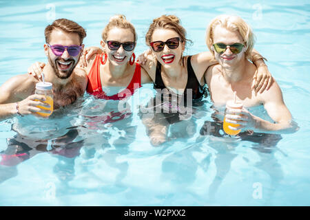 Portrait of a group of happy friends standing together in the swimming pool, having fun drinking juice and enjoying the summer time Stock Photo