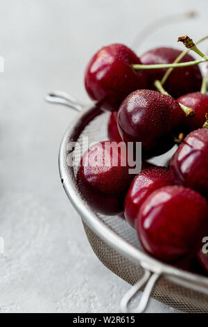 Close up sweet cherry in strainer with drops of water on gray background. Concept of summer raw food. Stock Photo