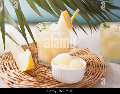 Glasses with melon cocktail with straw on a white table with palm leaf in tropical theme Stock Photo