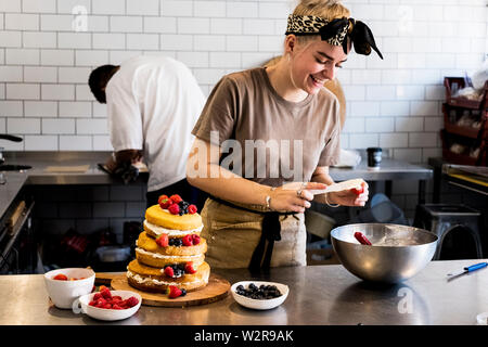A cook working in a commercial kitchen assembling a layered sponge cake with fresh fruit. Stock Photo