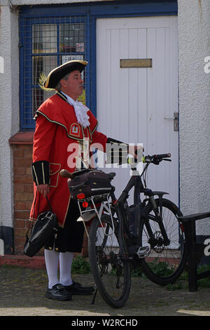 Watchet town crier in England, dressed in traditional red coat and black tricorn hat standing with his bicycle Stock Photo