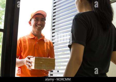Customers come out to pick up the parcel at the door from the delivery staff. Deliveryman smiling to received woman in front of home. Courier service Stock Photo