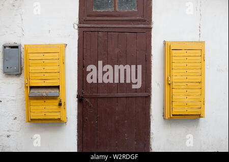 old retro vintage exterior white wall with wood door with lock and yellow opened mail boxes Stock Photo