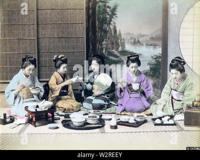 [ 1890s Japan - Women Having a Meal ] —   Having a meal. Five young women in kimono are seated on the floor. Two women are using chopsticks, one is pouring sake (rice wine) into the cup of the woman next to her, while the fifth is pouring tea.  19th century vintage albumen photograph. Stock Photo